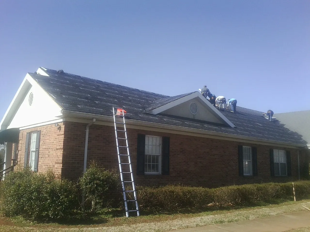 Crew tearing shingles off a brick ranch roof with a ladder set — Emergency Roof Repair work by our crew in Helenville