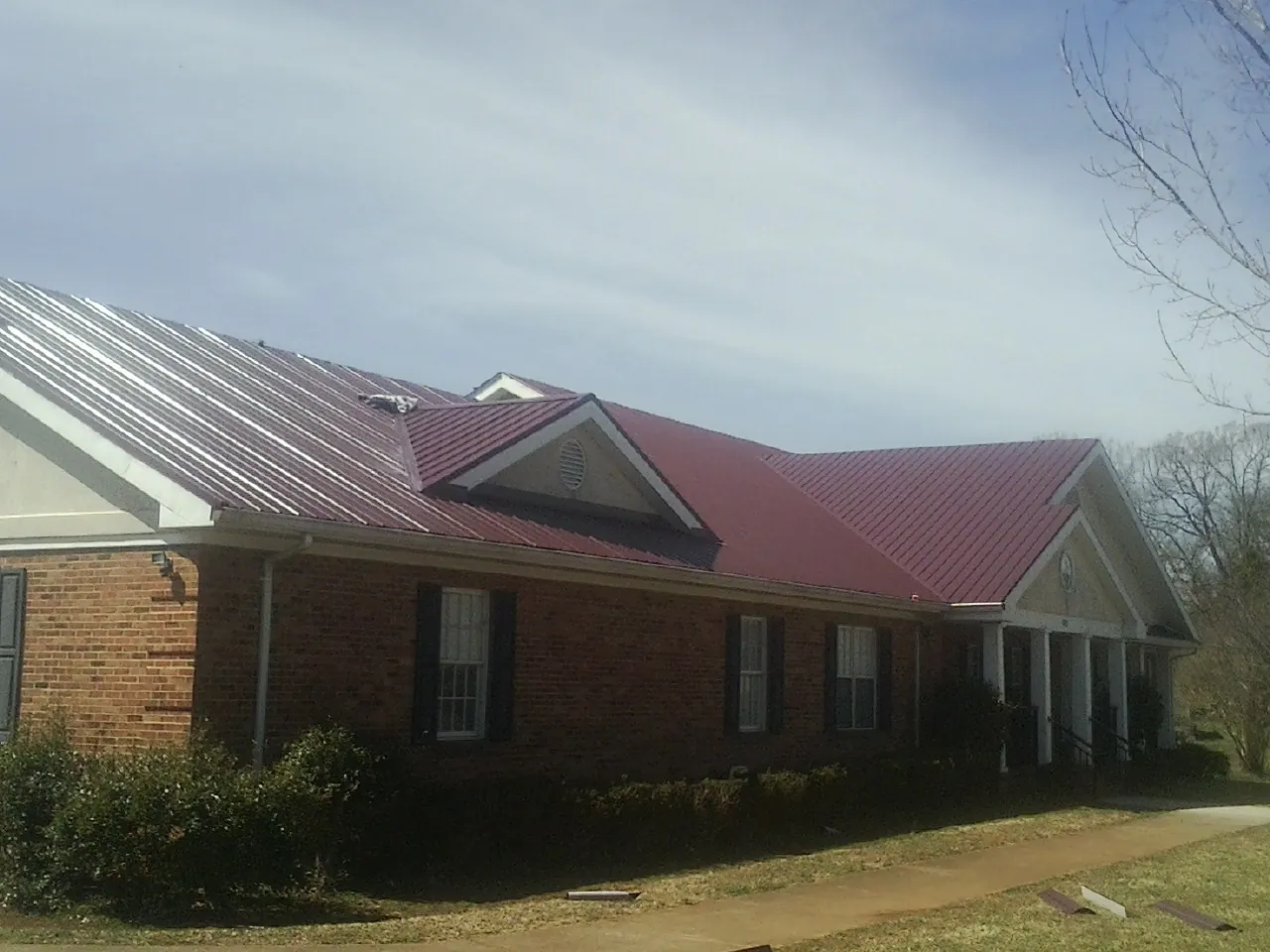 Red metal roof with gabled entries on a long brick building, from a Hail Damage Roof Repair job in Helenville