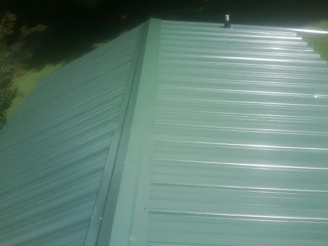 New green metal panels meeting at the ridge of a roof — Flat Roof Repair work by our crew in Helenville
