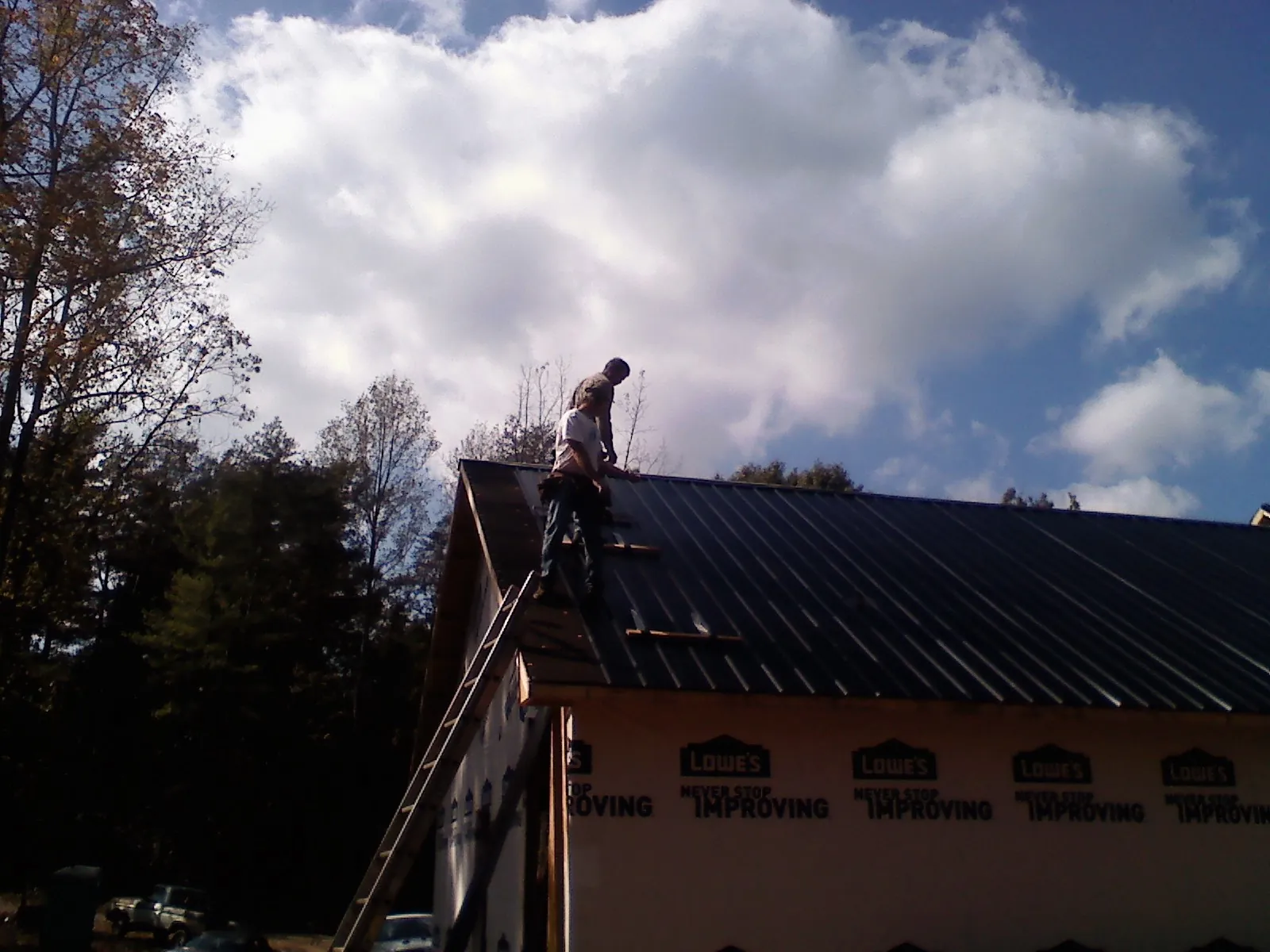 Roofer fastening dark metal panels high against a cloudy sky, from a Roof Inspection job in Helenville