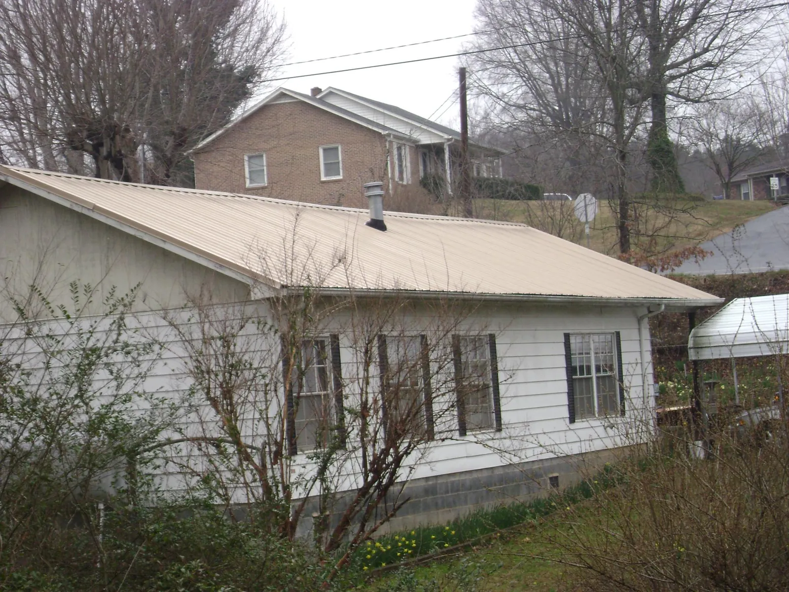 Tan metal roof on a white sided house set into a hillside — Commercial Roofing by Roofing Brothers in Helenville
